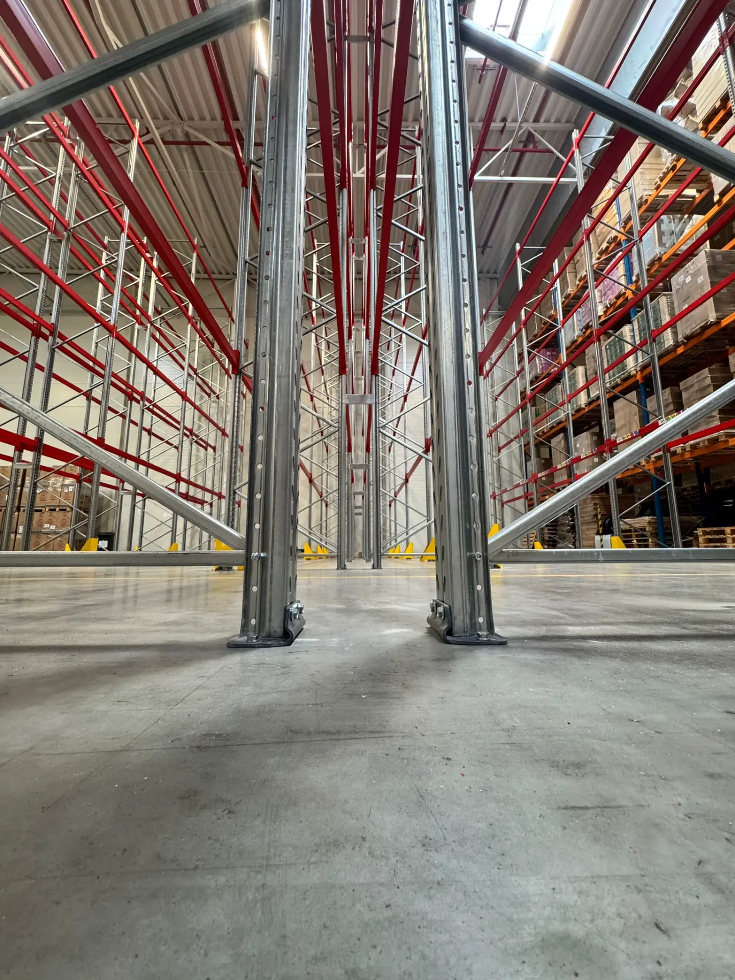 Langowski Logistics Łódź: Nowy magazyn z wysokimi regałami paletowymi i czerwonymi belkami, widok z poziomu posadzki.