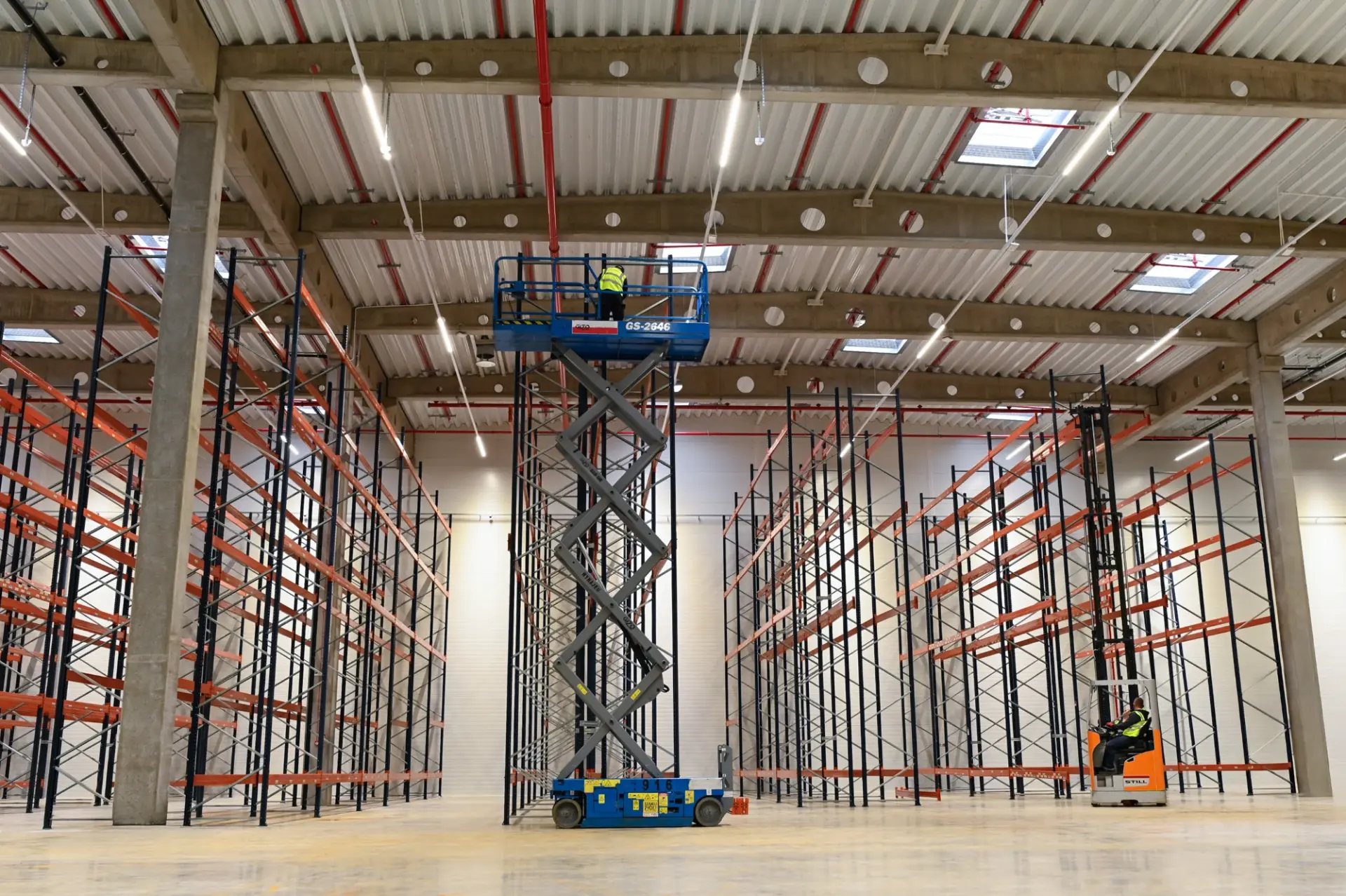 Langowski logistics Pruszków: Pracownicy przygotowują magazyn z pustymi regałami, jeden na podnośniku, drugi na wózku widłowym.