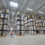 Langowski logistics Pruszków: Rozległy magazyn z rzędami regałów wypełnionych paletami, pracownik w kamizelce idzie.