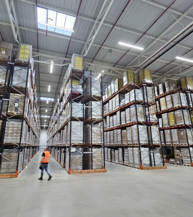 Langowski logistics Pruszków: Rozległy magazyn z rzędami regałów wypełnionych paletami, pracownik w kamizelce idzie.