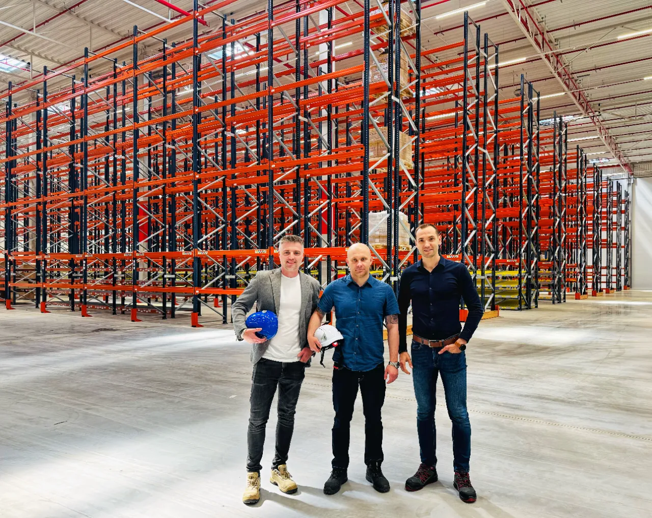 Yusen Logistics Polska: Trzech mężczyzn w magazynie z regałami paletowymi i zapasem w tle.