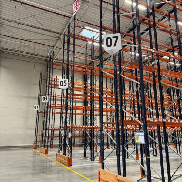 Yusen Logistics Polska: Wnętrze pustego magazynu z rzędami pomarańczowo-czarnych regałów, żółty podnośnik.