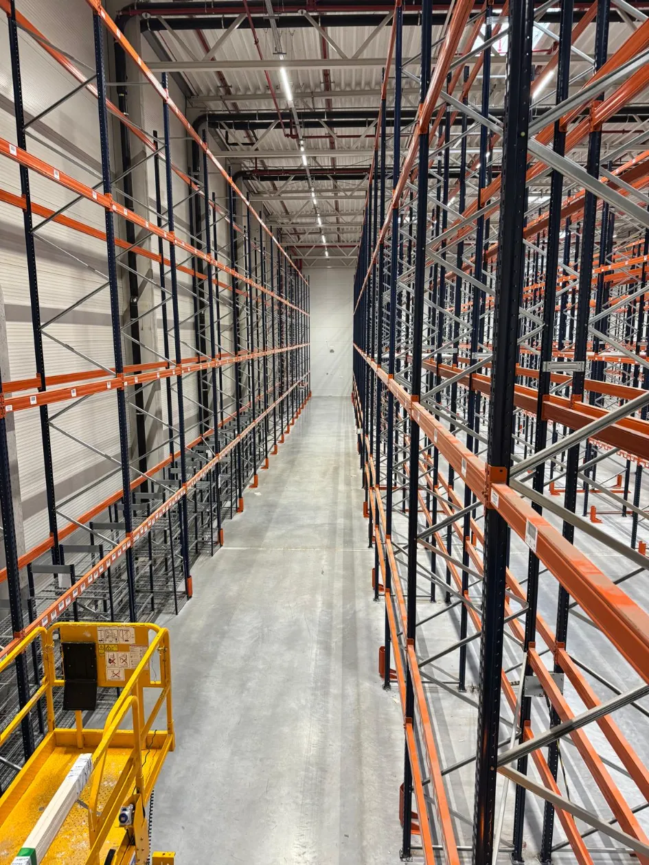 Yusen Logistics Polska: Wnętrze magazynu z pustymi, pomarańczowo-czarnymi regałami paletowymi i numerami alejek (01-07).
