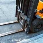 ile palet wejdzie na tira - Pomarańczowy wózek widłowy z czarnymi widłami i oponą na asfalcie. Napis: PALETOWE.PL.