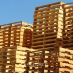 rodzaje palet: Wysokie stosy drewnianych palet na tle błękitnego nieba. Widoczny tekst: "PALETOWE.PL".