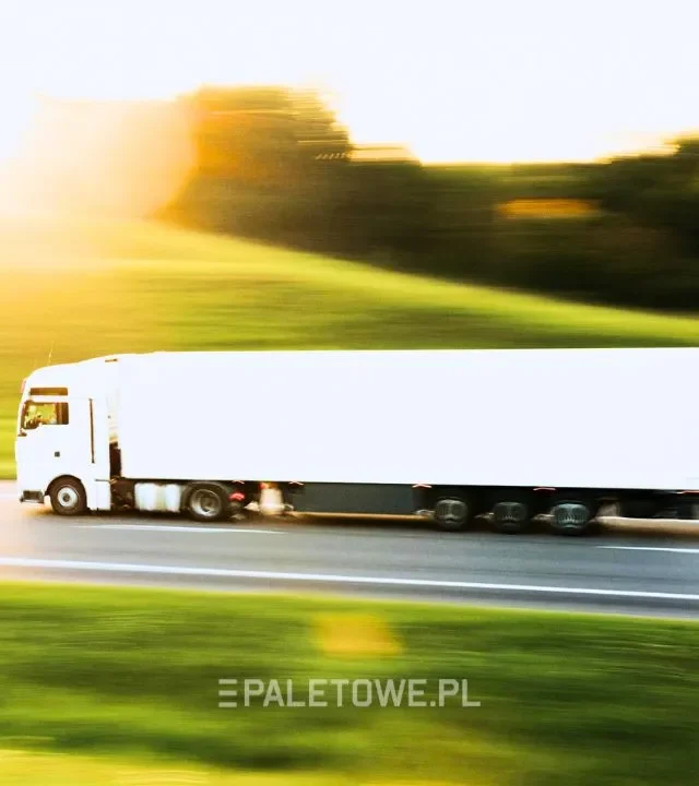 Wymiary naczepy tira – Biała ciężarówka z naczepą jedzie drogą w słoneczny dzień. Tło: zielone wzgórza, zamazane.